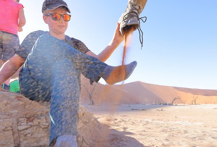 Namibia Familienreise im 4x4 Mietwagen mit Dachzelt - Sossusvlei - Junge schüttet Sand aus Schuhen